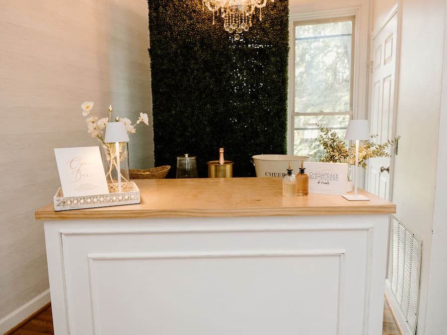 Elegant wedding bar setup with boxwood hedge wall and chandelier by Chesapeake Bartenders