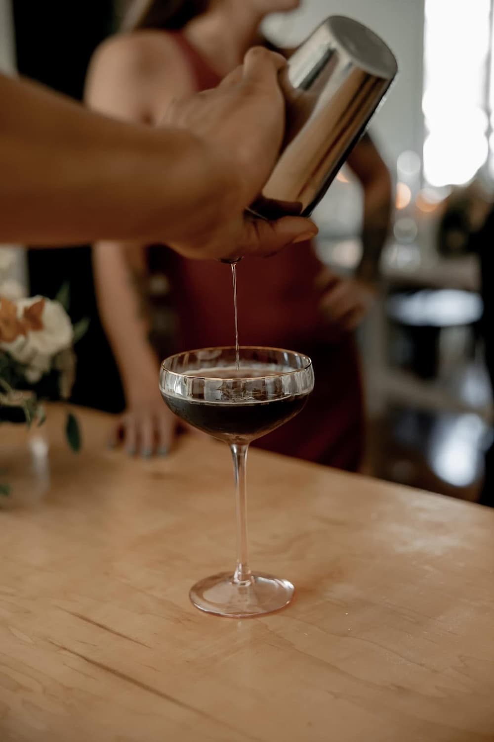 Close up of a bartender pouring an espresso martini into a coupe glass.